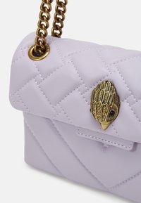 Světle fialová kožená kabelka s prošívaným vzorem, zlatým řetězovým popruhem a ozdobným zlatým uzávěrem ve tvaru ptáka.