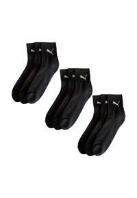 Drei Sets von drei schwarzen Knöchelsocken mit weißen Puma-Logos am Abschluss sind vor einem weißen Hintergrund ausgestellt.