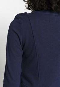 Mörkblå sweatshirt med en mjuk textur och åtsittande design, med synliga axelsömmar och en subtil sömdetalj längs ryggen.