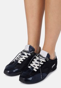 Navy blue sneakers with a mix of shiny patent leather and soft fur-like texture. Features white laces and black rubber soles.