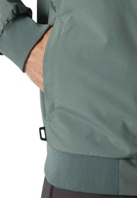 Chaqueta gris-verde con una textura suave y lisa, puños acanalados y un dobladillo ajustable con un gancho para un ajuste seguro.