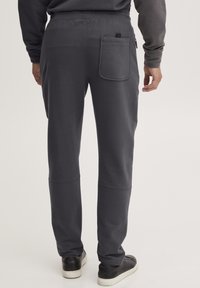 Grå joggebukser laget av mykt stoff, med en baklomme og en avsmalnende design, kombinert med svarte sko for kontrast.