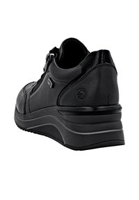 Chaussure en cuir noir avec un orteil arrondi, fermeture éclair et accents texturés. Semelle épaisse et plateformée avec une forme courbée et un fond patiné.