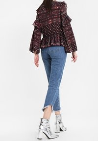 Blusa peplum nera con motivo e maniche a balze, abbinata a jeans azzurri e stivaletti argentati lucidi. Orlo sfilacciato sui jeans.