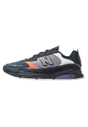 Men's athletic sneaker with black, gray, teal mesh, white and orange accents, black sole with purple detail, and large "N" logo on side.