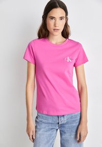 Roza pamučna majica s kratkim rukavima, okruglim izrezom i malim bijelim logotipom Calvin Klein na lijevoj strani prsiju. Glatka tekstura, prilagođeni dizajn.