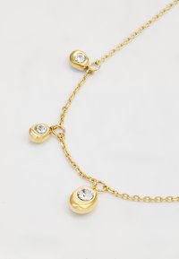Gouden ketting met drie afgeronde hangers, elk met een centrale heldere rhinestone, aan een delicate ketting. Smooth textuur, glanzende afwerking.