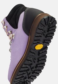 Purple suede hiking boot with black accents, metal hooks, and a textured rubber sole featuring a logo and aggressive tread for traction.