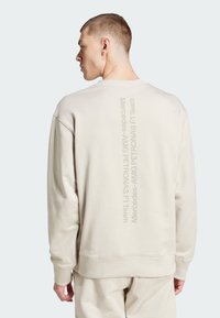 Sudadera beige con cuello redondo, que presenta un texto impreso vertical "Mercedes-AMG PETRONAS F1 Team" en la parte posterior. Tejido suave de mezcla de algodón.