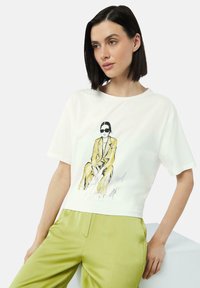 Weißes Baumwoll-T-Shirt mit kurzen Ärmeln, das eine gelbe illustrierte Figur in einem Anzug und Sonnenbrillen zeigt, mit silbernem Text darunter.