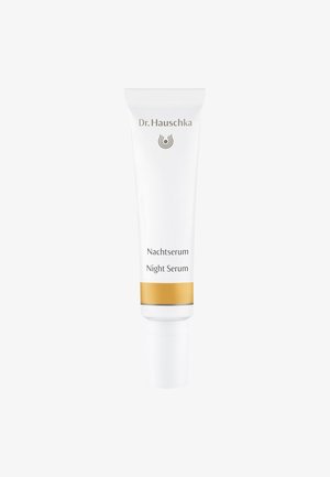 Tubetto bianco di Dr. Hauschka Night Serum con una fascia accentuata dorata, caratterizzato da un testo semplice e una punta arrotondata per il dosaggio del prodotto.