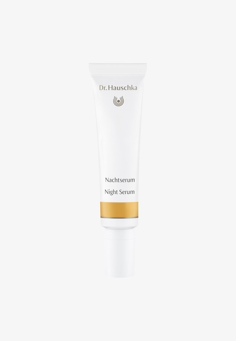 Tube blanche de sérum de nuit Dr. Hauschka avec une bande d'accent dorée, présentant un texte simple et un embout arrondi pour le dosage du produit.