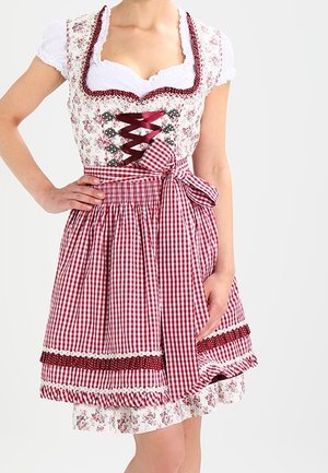 Kvinde iført en hvid bluse med en blomsterbroderet snørebodice og et rødt og hvidt ternet skørt bundet med en sløjfe i taljen.