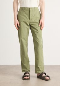 Light green cotton trousers with a straight cut, featuring a front button closure and side pockets, paired with dark sandals.