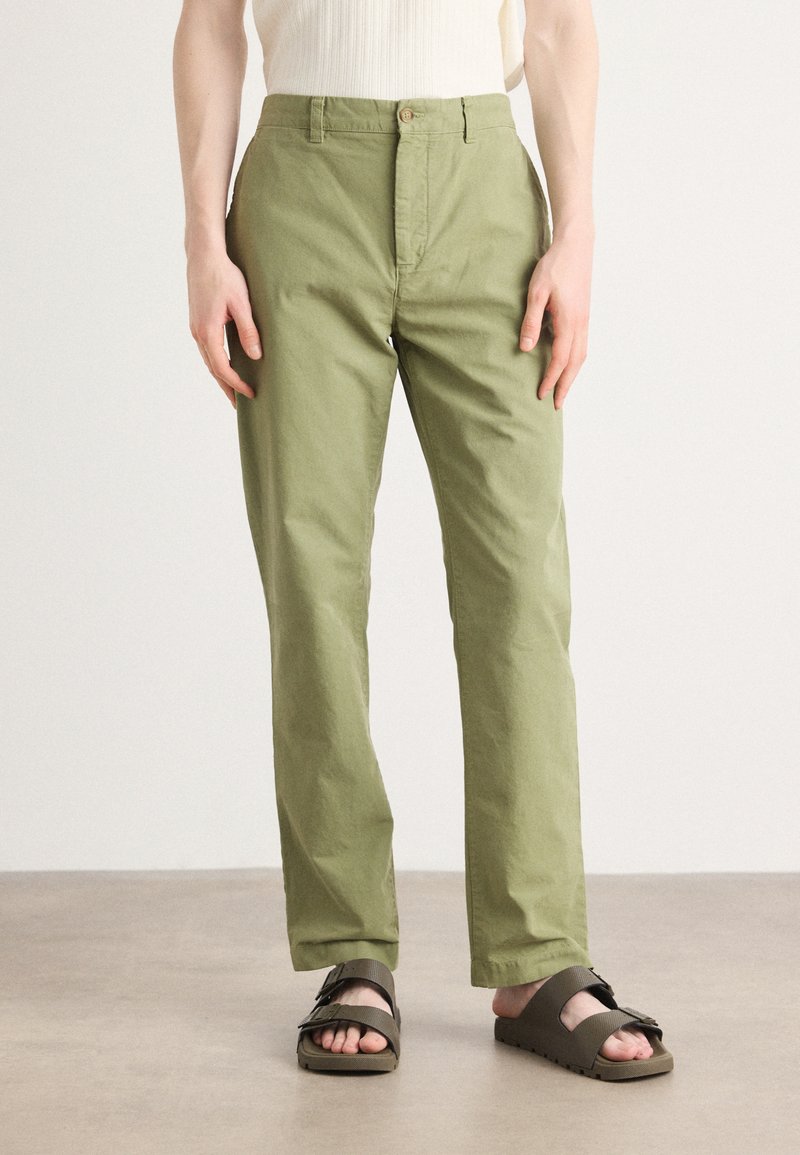 Light green cotton trousers with a straight cut, featuring a front button closure and side pockets, paired with dark sandals.