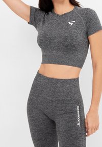 Crop top atletico grigio con maniche corte, caratterizzato da un tessuto texturizzato e un logo bianco sul petto. Abbinato a leggings a vita alta coordinati.