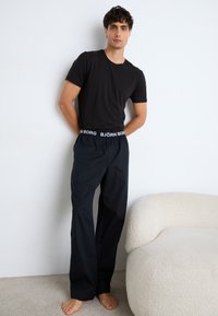 Camiseta preta combinada com calças largas pretas com uma cintura elástica com o logo branco "BJÖRN BORG". Textura suave, design minimalista e sem padrões visíveis.
