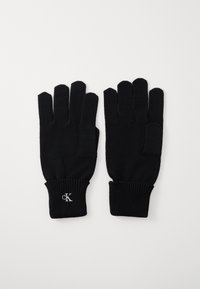 Mustad mustad sõrme kindad, viie sõrmega, soonilise varrukaosaga ja väikese valge "cK" logoga randme piirkonnas. Pehme tekstuur ja liibuva disain.