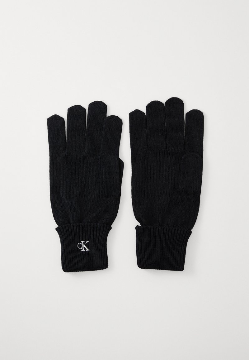 Mustad mustad sõrme kindad, viie sõrmega, soonilise varrukaosaga ja väikese valge "cK" logoga randme piirkonnas. Pehme tekstuur ja liibuva disain.