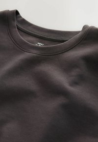 Prim-plan al unui sweatshirt maro închis cu guler rotund, cu cusături vizibile și textură moale a țesăturii.