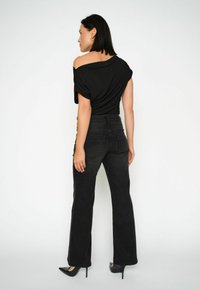 Top nero scollato con spalle scoperte e maniche arrotolate, abbinato a jeans flare in denim nero a vita alta. Tessuto morbido, design minimalista.