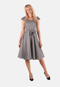 Schwarz-weißer Karodress mit kurzen Ärmeln, tailliertem Schnitt und knielanger Rocklänge, der vorn mit einem gebundenen Detail versehen ist.