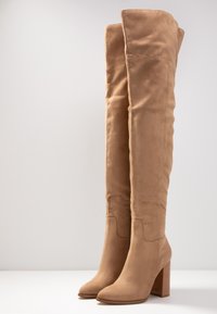 Beige stövlar över knäna i mjukt mocka med en slät yta, med en kraftig träklack och en rund tådesign.