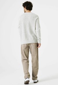 Hellgrauer Strickpullover mit Sprenkeln, rundem Ausschnitt und gerippten Bündchen, kombiniert mit beigen Cordhose und weiß-schwarzen Sneakers mit Streifen.