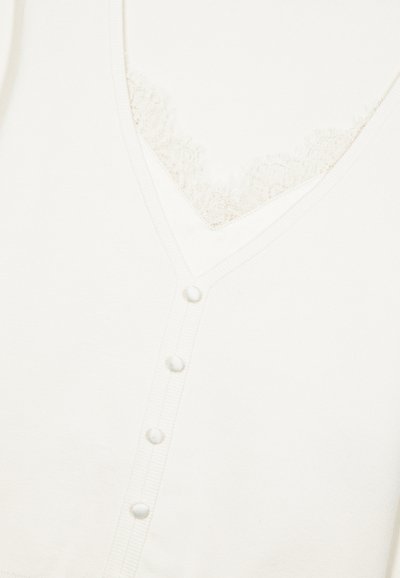 Hvid v-hals top lavet af blødt stof med blonderkant under halsudskæringen og seks matchende knapper langs frontknaplisten.