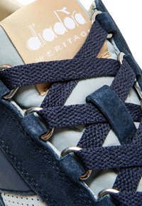 Sneaker blu navy realizzato in materiali scamosciati e tessili, con lacci testurizzati e etichetta del logo, che mostra occhielli e dettagli di cucitura intricati.