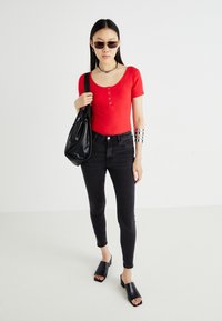 Piros bordás, rövid ujjú felső gombos részletekkel, fekete skinny farmernadrággal és fekete nyitott orrú, blokkkilincsű papuccsal párosítva; fekete válltáska.