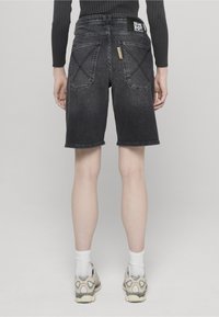 Pantalones cortos de mezclilla negra con un ajuste relajado, que cuentan con dos bolsillos traseros con detalles de costura cruzada y una etiqueta con el logo en la cintura.