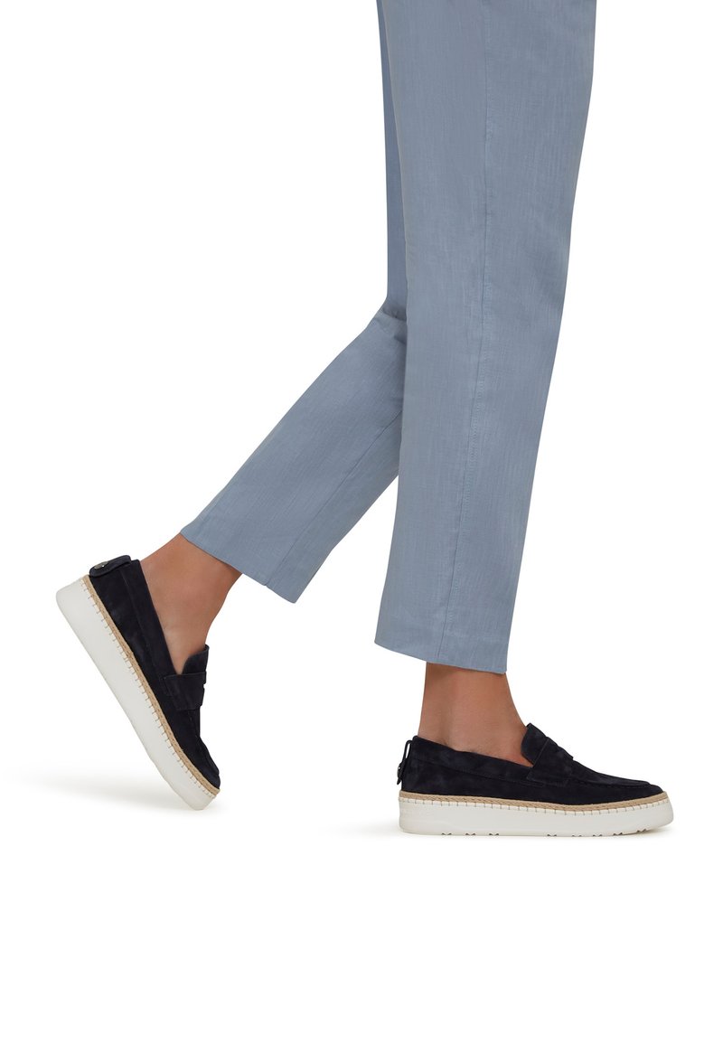Czarne suede buty typu slip-on z białą gumową podeszwą i plecionym wykończeniem. Noszone z krótkimi jasnoniebieskimi spodniami, podkreślającymi komfort noszenia.