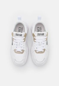 Bílé sportovní tenisky s hladkým koženým svrškem, kovovými zlatými akcenty, silnými tkaničkami a polstrovaným límečkem pro pohodlí.