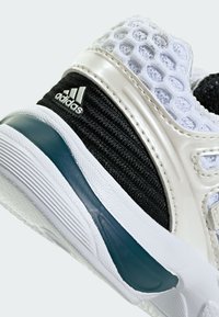 Gros plan sur la zone du talon d'une basket Adidas blanche et noire avec tissu en mesh et un accent bleu sur la semelle.