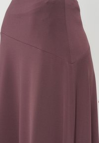 Jupe taille haute mauve avec détail de couture diagonale et tissu lisse et fluide en gros plan.