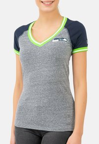 T-shirt gris à col en V avec des manches courtes bleu marine et des accents vert lime. Présente un logo des Seattle Seahawks sur la poitrine. Texture douce.