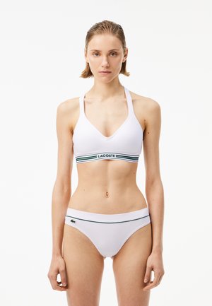 White bikini set featuring a V-neck bralette with a striped band and matching low-rise bottoms with a logo accent. Smooth texture, minimal design.