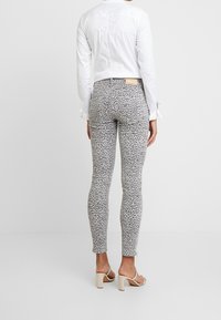 Jeans ajustados con estampado de leopardo en gris y negro, con una textura suave, combinados con una camisa blanca corta de botones y sandalias de tacón cuadrado beige.