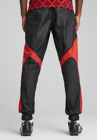 Svarte og røde joggebukser laget av lett materiale, med kantede røde detaljer, elastiske mansjetter og en tapered passform. Egnet for sport.
