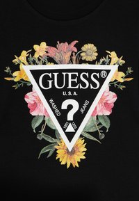 Tricou negru cu un logo triunghiular ce conține cuvântul "GUESS" și motive florale în nuanțe de roz, galben și verde. Detalii strălucitoare în jurul logo-ului.