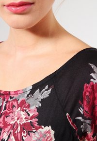 Haut noir floral avec un décolleté en scoop, arborant des motifs de fleurs roses, rouges et grises. Tissu doux avec une texture lisse.