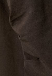 Tessuto marrone con una texture morbida e liscia, che presenta lievi pieghe e una leggera lucentezza. La superficie sembra elastica e aderente.