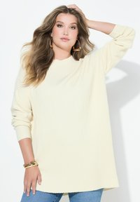 Krémový žebrovaný svetr s vysokým výstřihem a dlouhými rukávy, doplněný modrými džíny. Vyznačuje se volným střihem a texturovanou tkaninou.