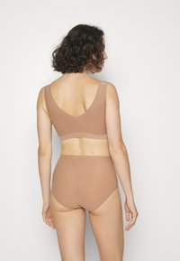 Beige nahtloser Bralette mit tiefem V-Rücken, breiten Trägern und passenden hochgeschnittenen Slips, die eine glatte, dehnbare Textur aufweisen.