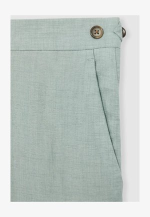 Jasnozielone lniane spodnie o gładkiej fakturze, z boczną kieszenią i brązowym guzikiem w talii. Swobodny, luźny fason.