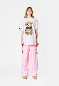 Camiseta rosa oversized con un gráfico de un oso de peluche, combinada con pantalones rosas holgados que presentan acentos de pompones. Tejido suave, ajuste relajado.