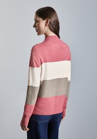 Stickad tröja med horisontella ränder i rosa, krämfärg och beige. Hög krage, ribbade ärmslut och nederkant. Mjuk textur. Bärs med mörkblå jeans.
