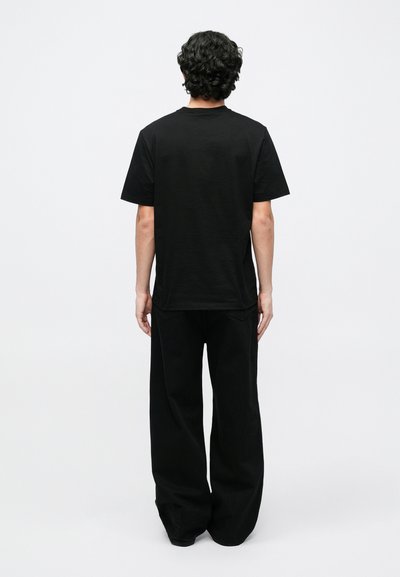 Μα�ύρο βαμβακερό t-shirt με κοντά μανίκια και στρογγυλή λαιμόκοψη, συνδυασμένο με μαύρο παντελόνι φαρδιάς γραμμής. Η πίσω όψη δείχνει άνετη εφαρμογή και μινιμαλιστικό σχεδιασμό.