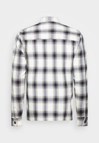 Langermige flanellen shirt met knopenmanchet in een wit, zwart en bruin ruitpatroon, weergegeven vanaf de achterkant op een lichtgrijze achtergrond.